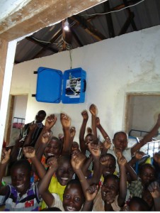 Students at a Ugandan orphanage school celebrate the installation of an outdoor electric light, with power supplied by a solar suitcase.
