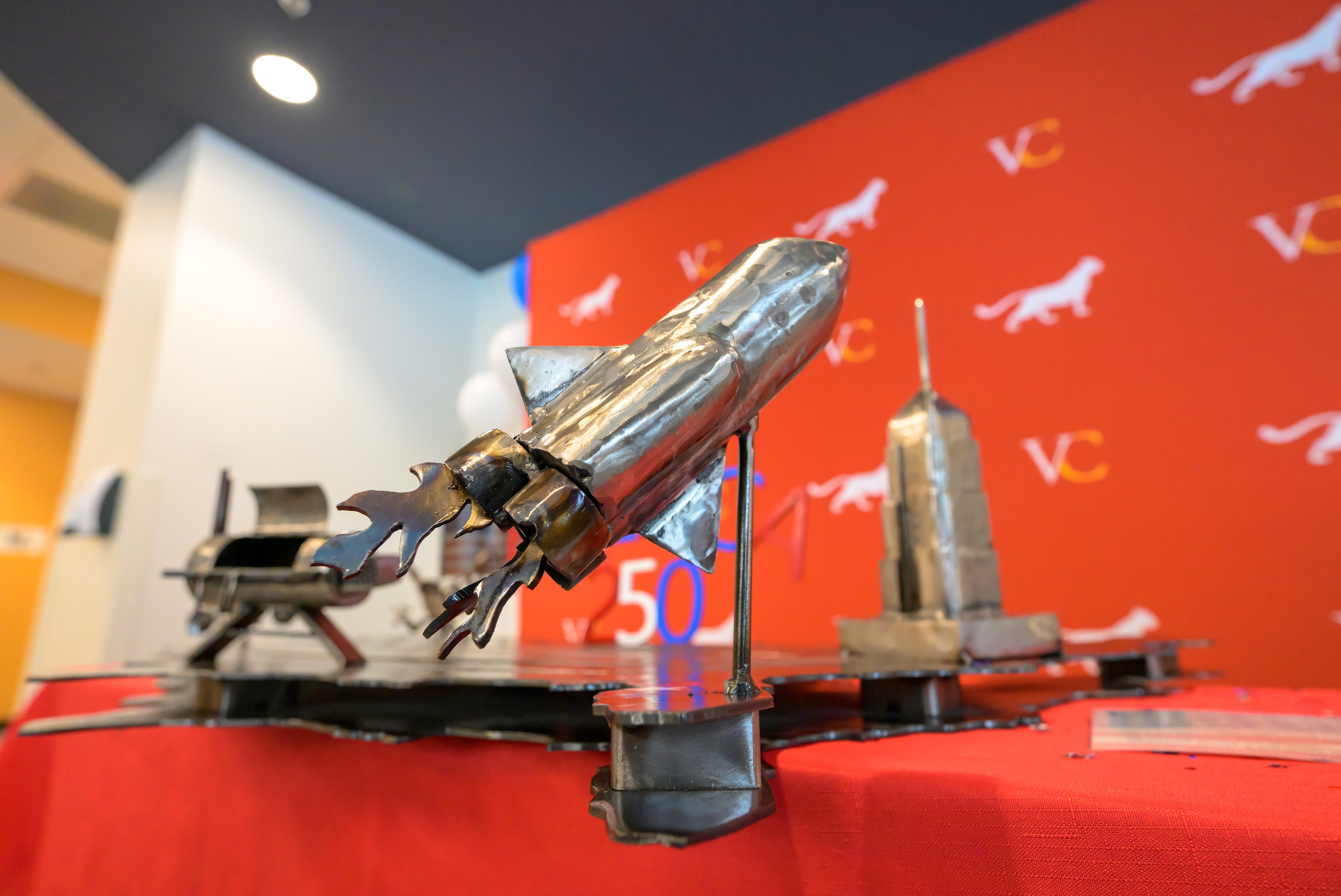 Photo shows a rocket fabricated from steel welded to a map of the United States, with a replica of the Empire State Building in the background.